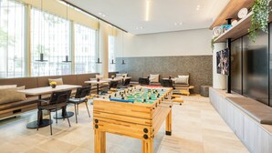 A modern indoor space with a foosball table, seating areas, and large windows. - Citadines Kurfürstendamm Berlin (Berlin)