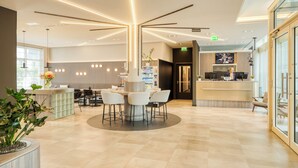 A modern reception area with a central round table, seating, a reception desk, and a television screen. - Citadines Kurfürstendamm Berlin (Berlin)