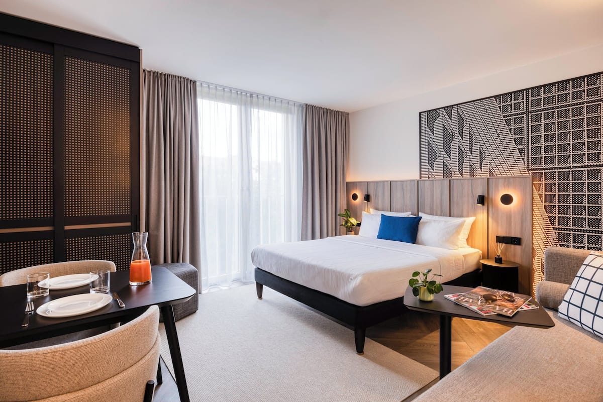 A modern hotel room with a large bed, a dining area, and a seating area.