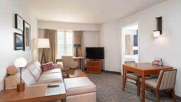 A hotel room with a sofa, a desk, a television, and a dining table with chairs.