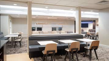 A modern dining area with booths and tables, carpeted flooring, and pendant lighting.