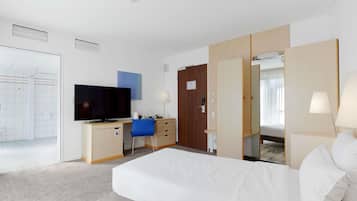 Ein Hotelzimmer mit Bett, Schreibtisch mit Fernseher, Stuhl, Kleiderschrank und Spiegel.