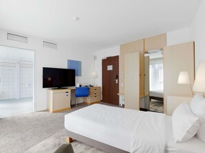 A hotel room with a bed, a desk with a TV, a chair, a wardrobe, and a mirror. - Novotel Berlin Mitte (Berlin)