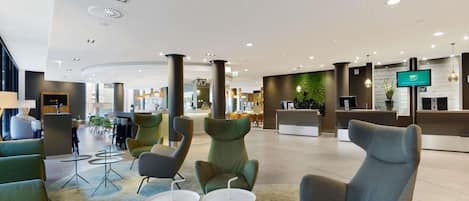 A spacious lobby with modern seating, a reception desk, and a large screen displaying information.