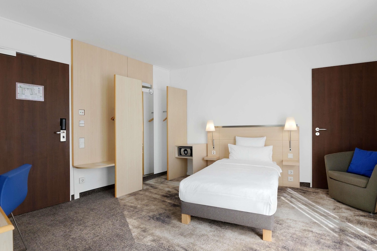 A hotel room with a bed, bedside lamps, a desk, a chair, and a wardrobe.