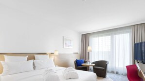 A hotel room with a large bed, a desk, a chair, a TV, and a window with curtains. - Novotel Berlin Mitte (Berlin)