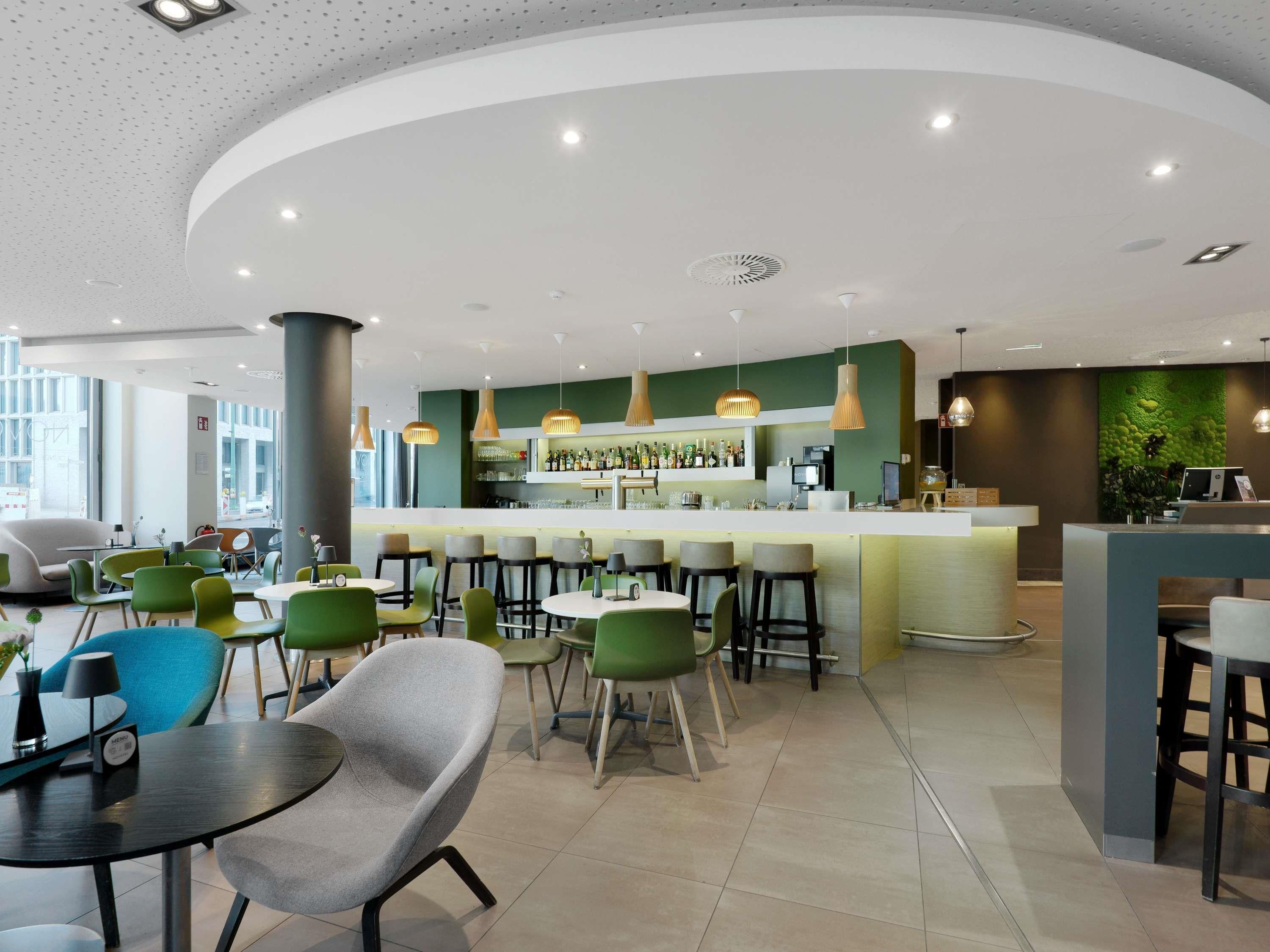Eine moderne Bar mit einer gebogenen Theke, grau-grünen Stühlen und einer grünen Wand mit strukturierter Gestaltung.