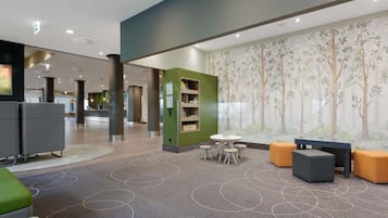 A modern lobby with a reception desk, seating areas, and a mural of trees.