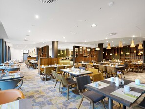Un amplio comedor de hotel con varias mesas y sillas, un bar central y un diseño de techo moderno.