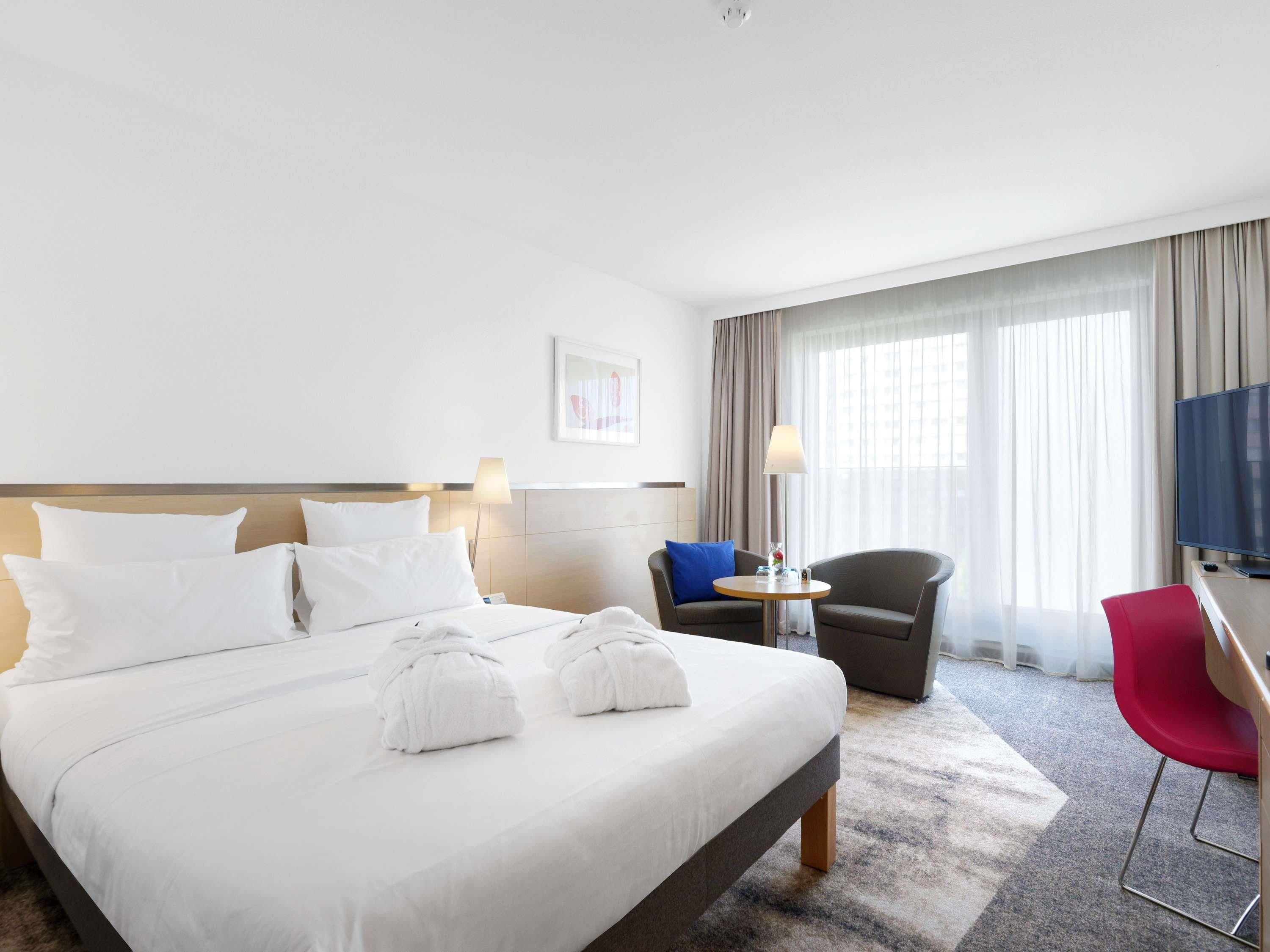 A hotel room with a large bed, a desk, a chair, a TV, and a window with curtains.