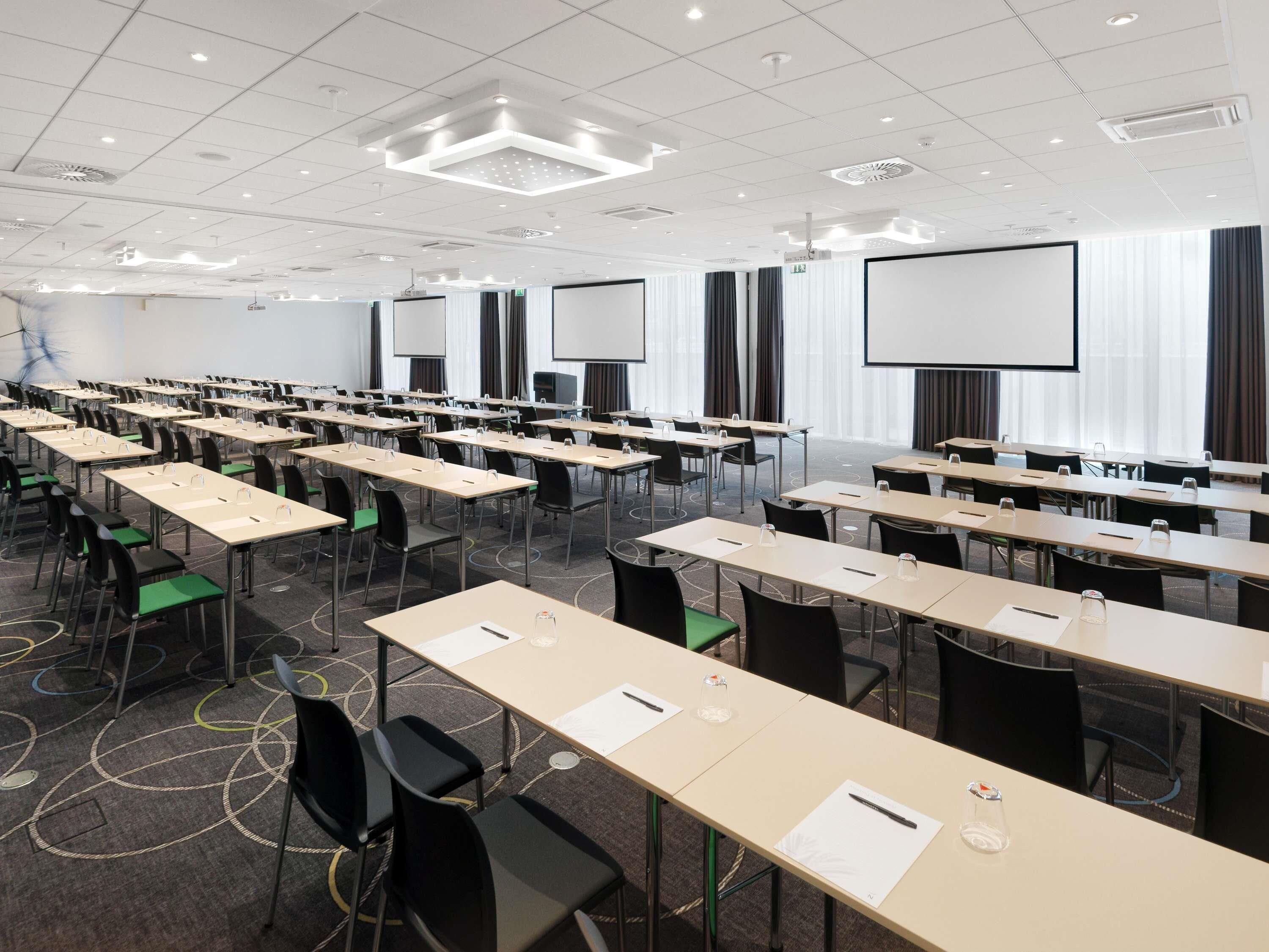 Ein Konferenzraum mit Tischen, Stühlen und einer großen Leinwand.