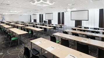 Ein Konferenzraum mit Tischen, Stühlen und einer großen Leinwand.