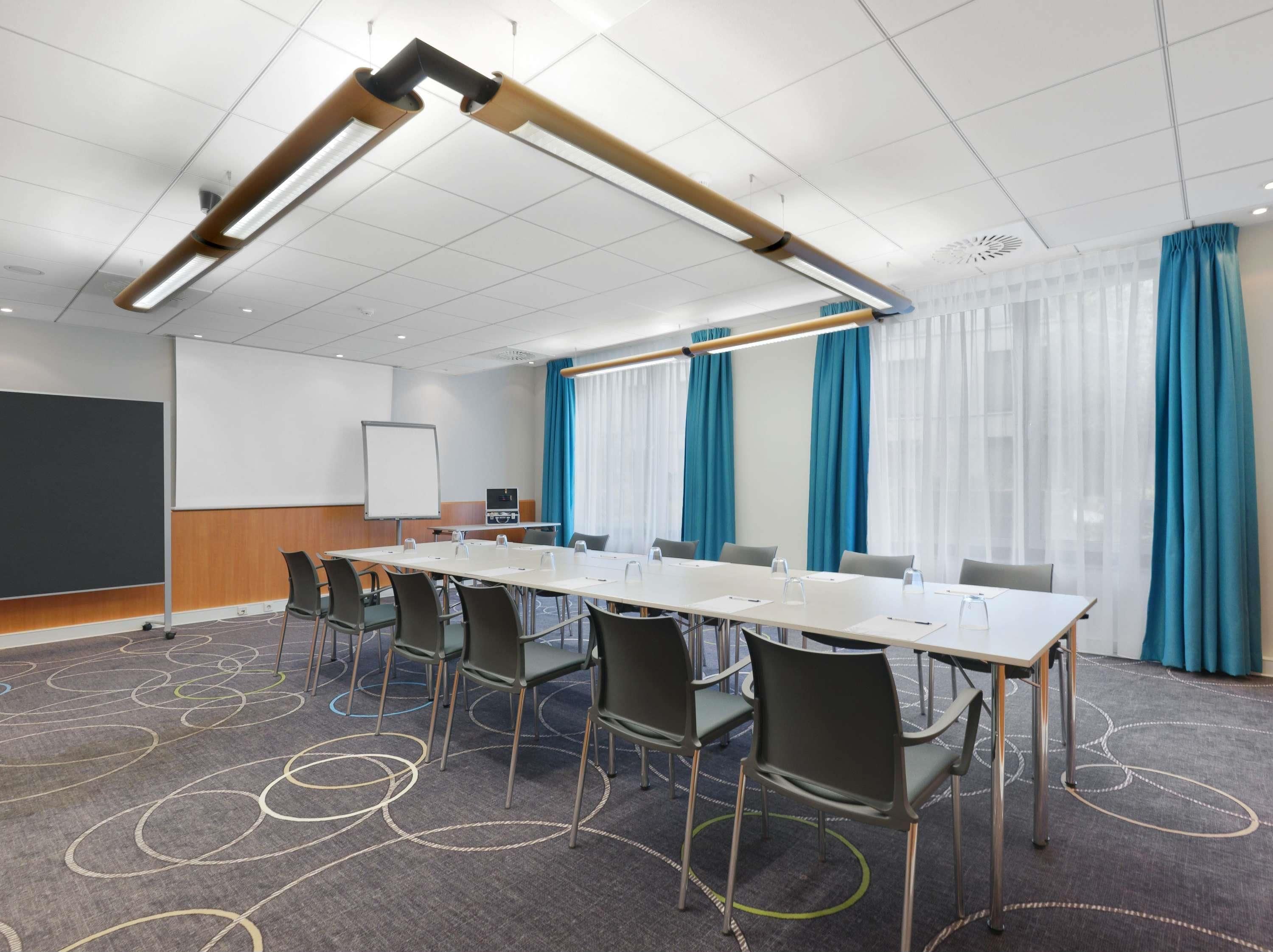 A conference room with a long table, chairs, a whiteboard, and a projector screen.