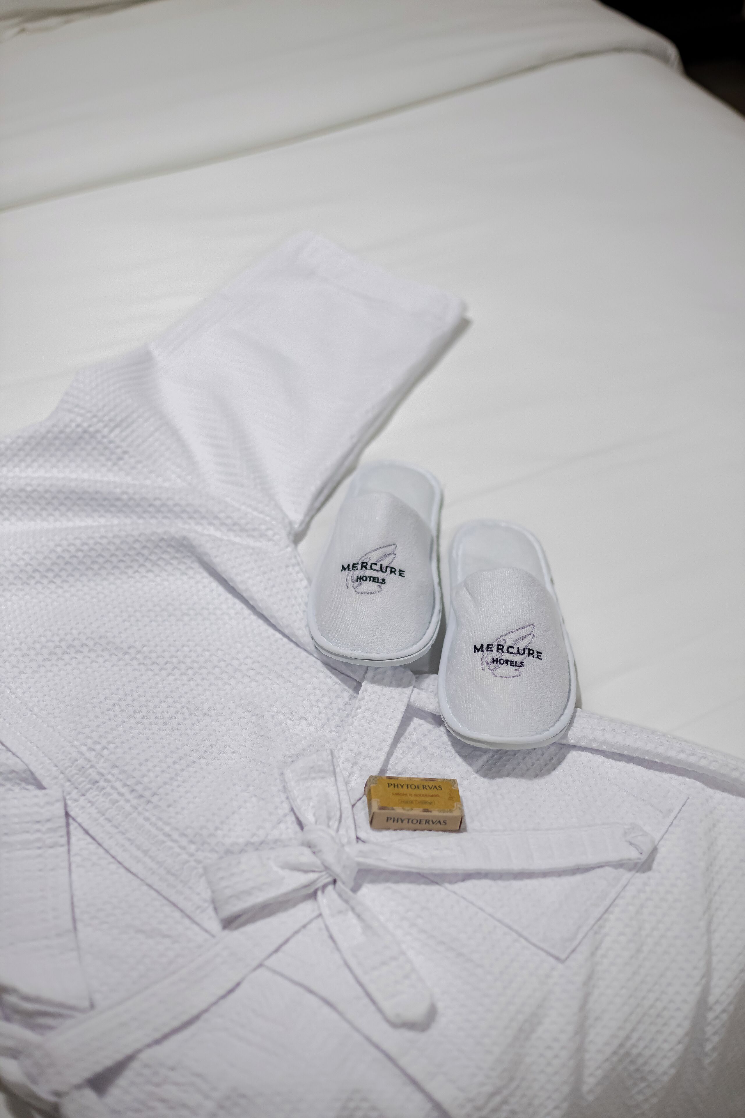 A neatly folded white bathrobe and slippers with 'Mercure Hotels' branding on a white bedspread.