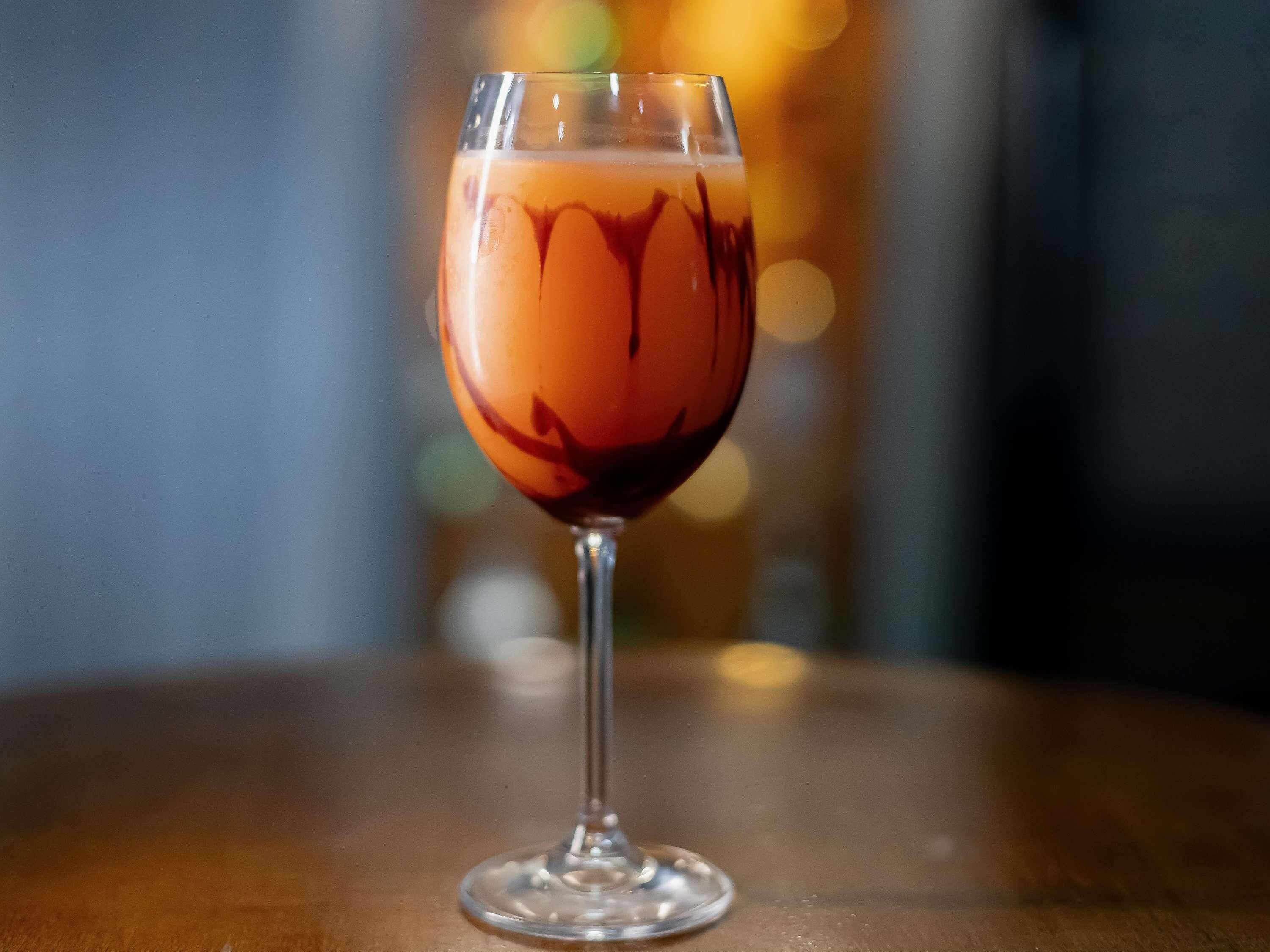 A clear glass with a dark liquid, possibly a cocktail, on a wooden surface.