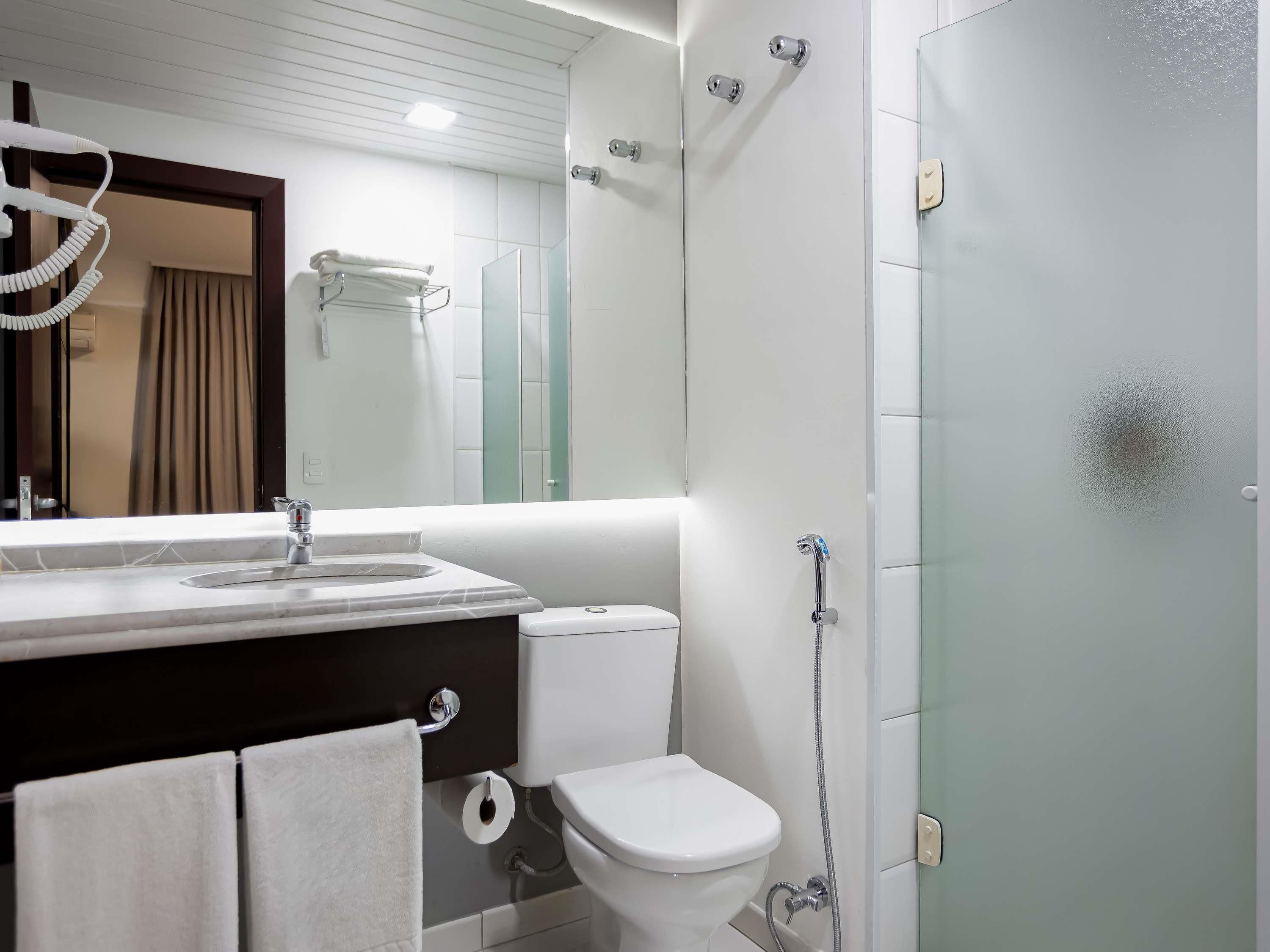 Casa de banho moderna com lavatório branco, sanita e cabine de duche em vidro.