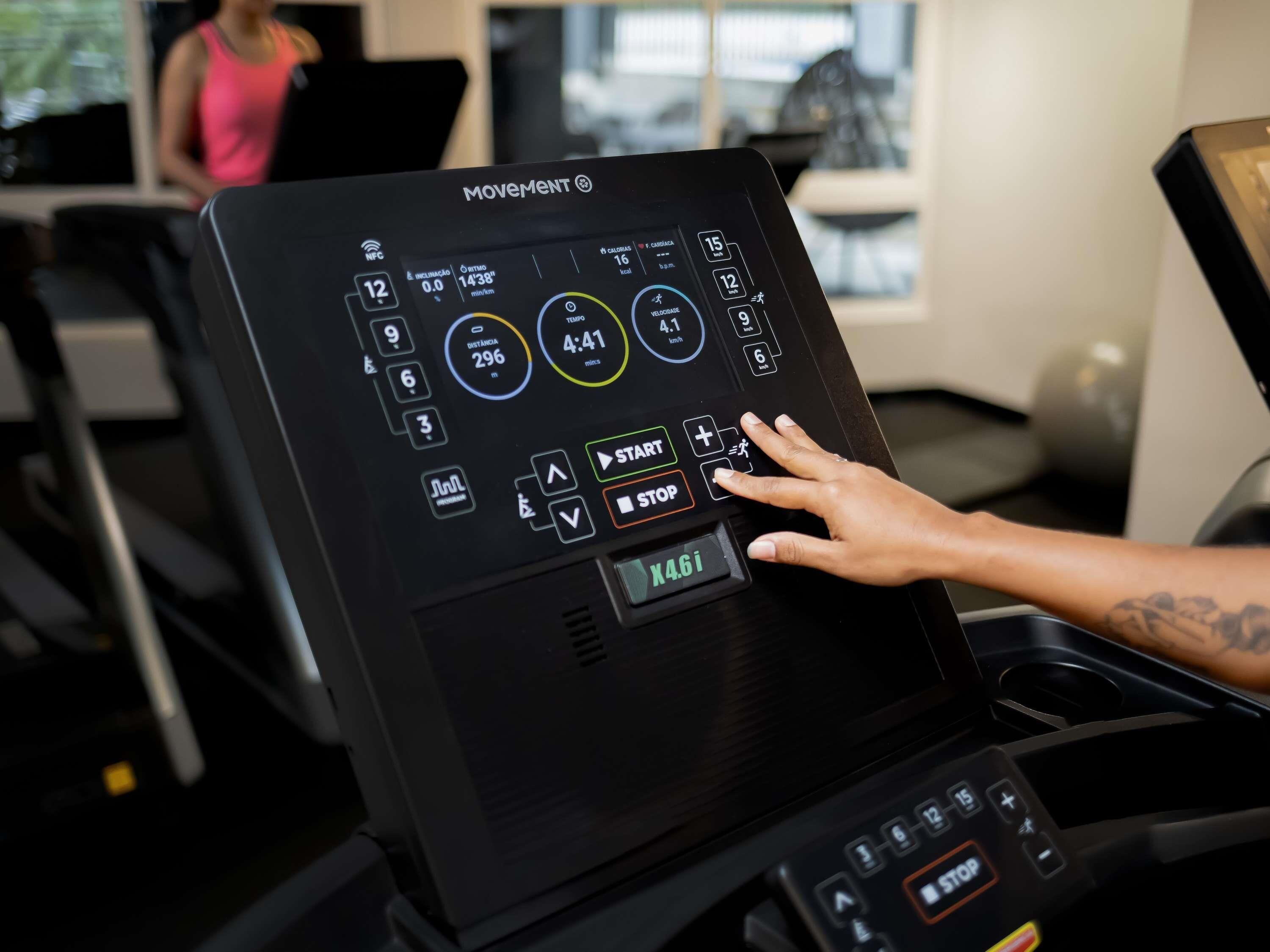 Panel de control de una cinta de correr con varios botones y pantallas, incluyendo un reloj digital y datos de distancia.