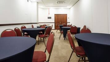 Una sala de conferencias con mesas redondas y sillas rojas, paredes blancas y una puerta de madera.