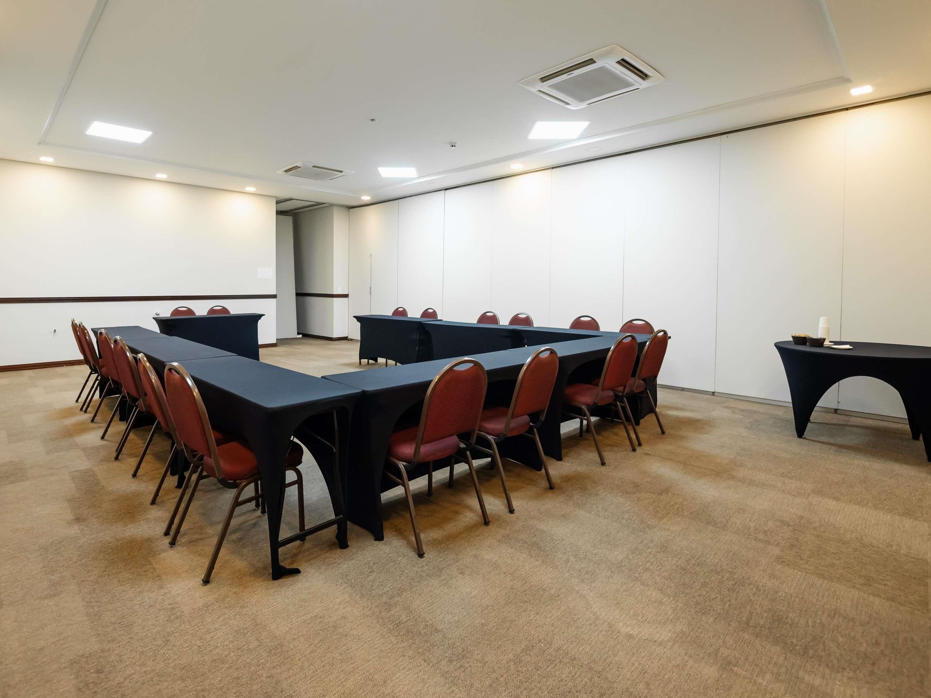 Una sala de conferencias con una larga mesa, sillas rojas y piso alfombrado.
