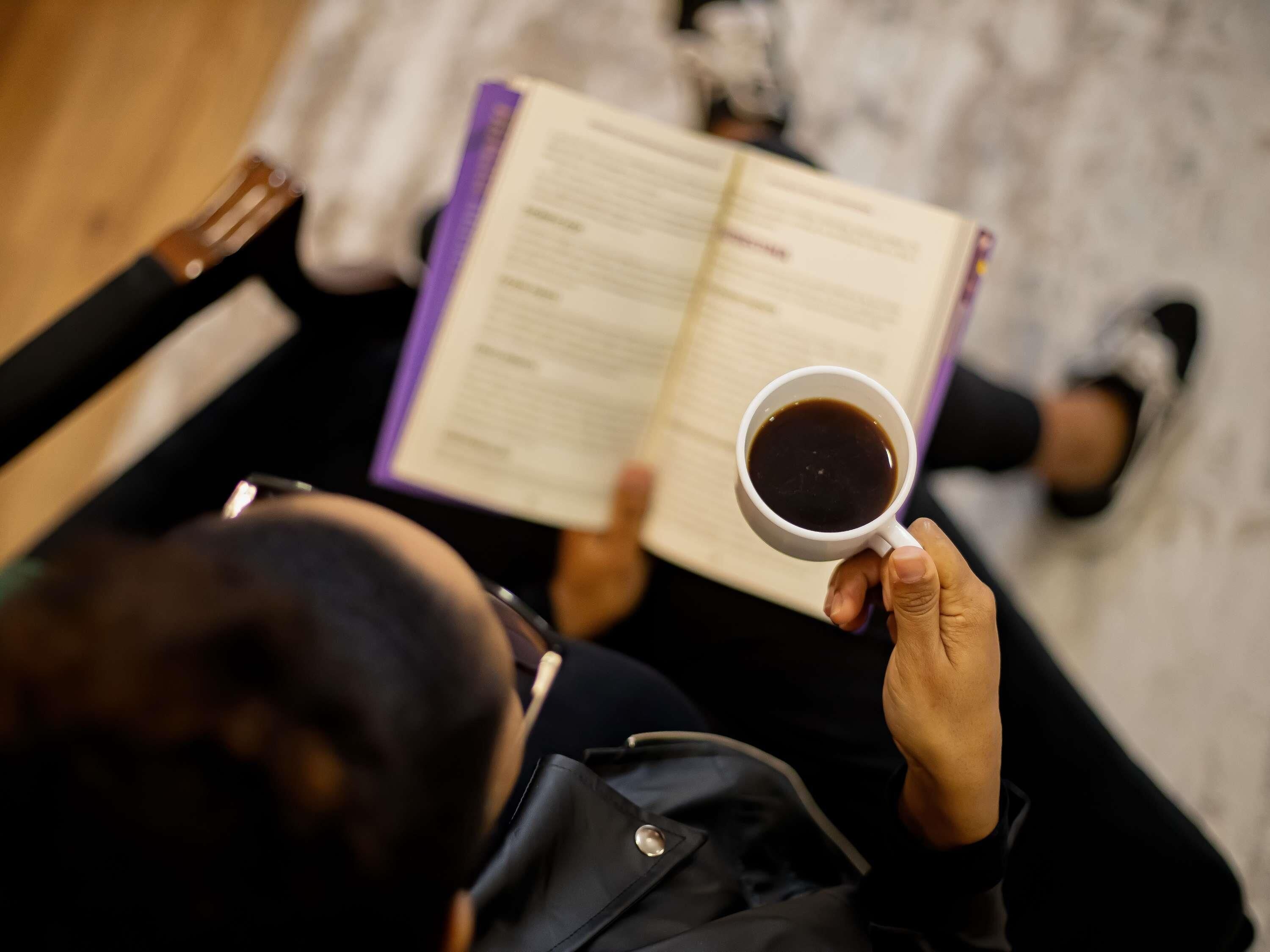 Uma pessoa lendo um livro com uma xícara de café.
