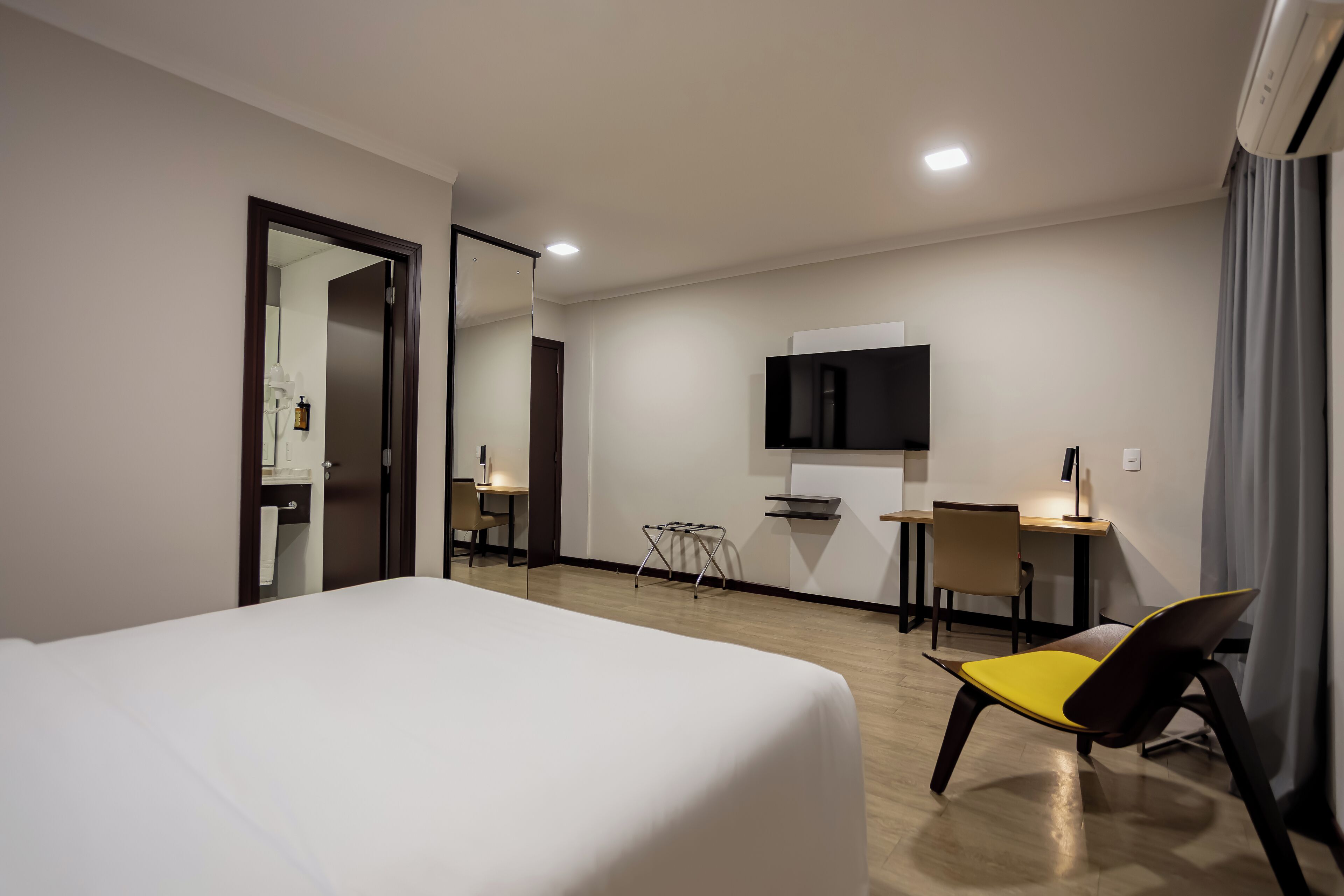 Una habitación de hotel con cama, escritorio, silla, televisión y espejo.