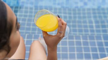 A person holding a glass of orange juice by a pool with a checkered pattern.
