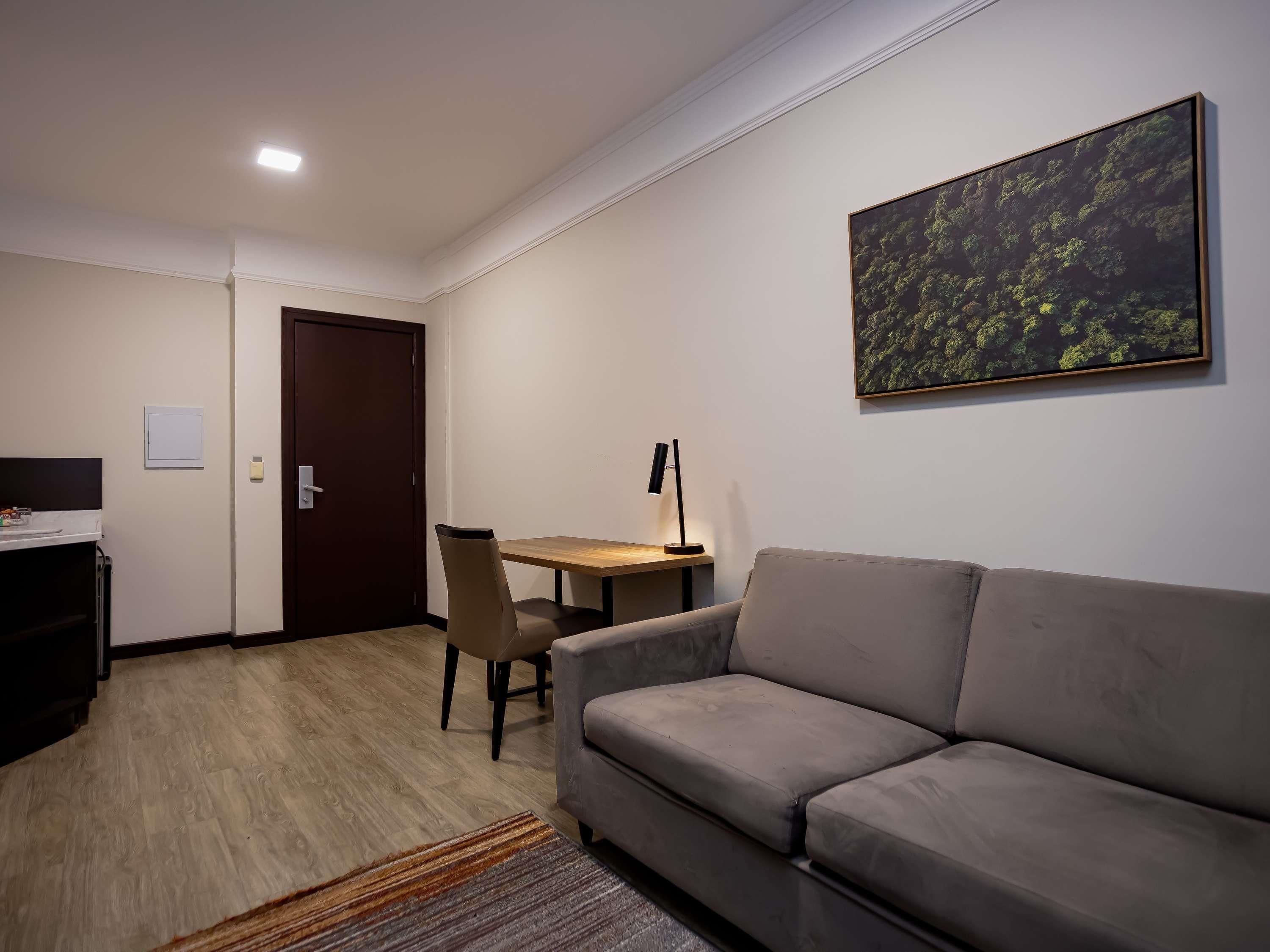 Uma sala de estar moderna com sofá, mesa de jantar com cadeira, um quadro na parede e uma porta.