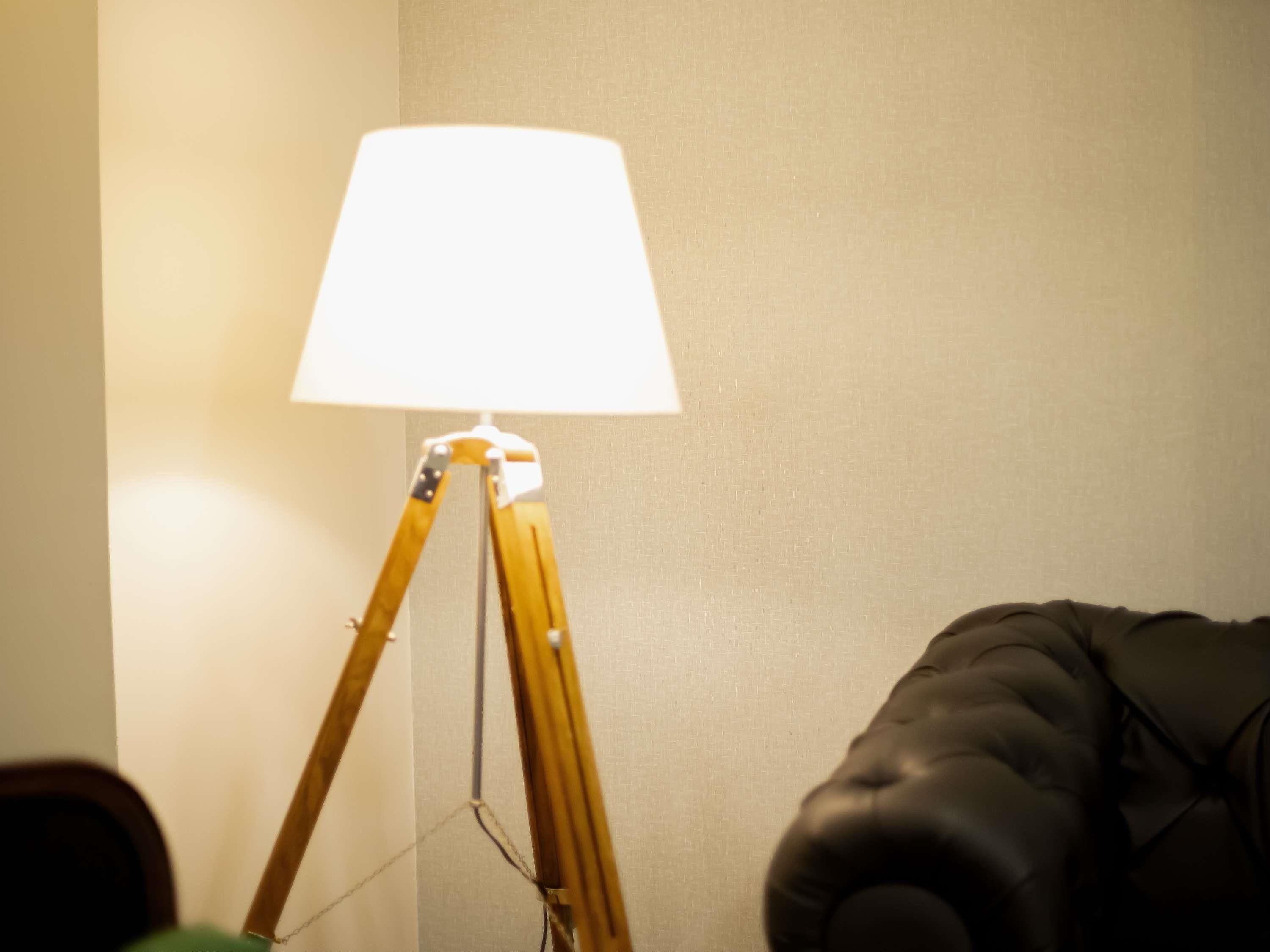 Un lampadaire avec un abat-jour blanc, un fauteuil en cuir marron et un mur à texture.