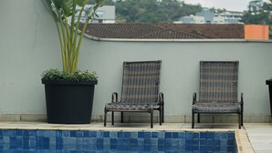 Una piscina con dos sillas de mimbre y una planta en maceta.