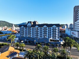 Hotel de vários andares com design moderno, apresentando varandas em cada andar, entrada imponente e vista para a área urbana ao redor.