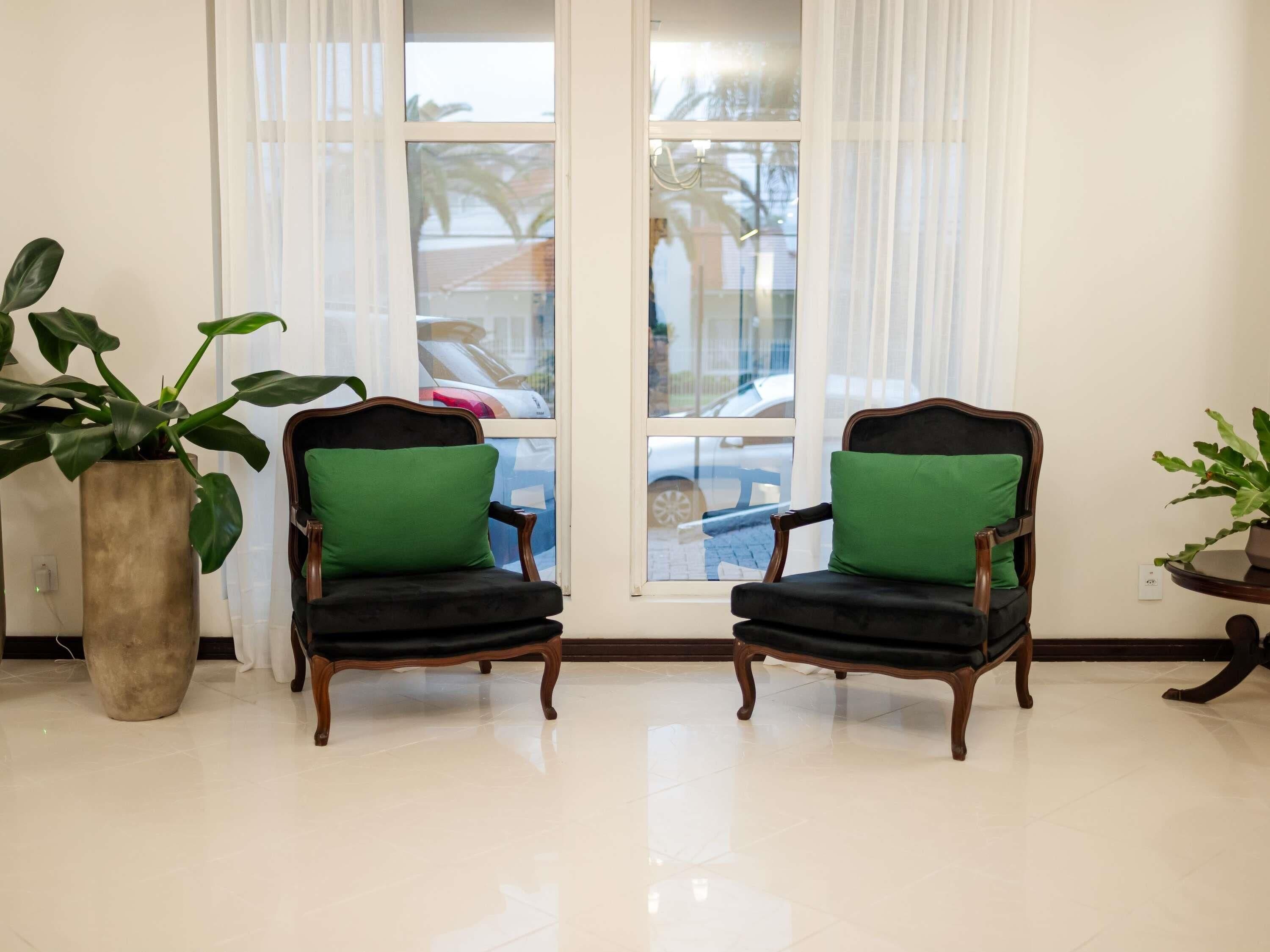 Dos sillones con cojines verdes orientados hacia un ventanal con vistas a una calle y coches aparcados.