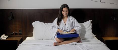 A person sitting on a bed in a hotel room, holding a tray with a plate of food.