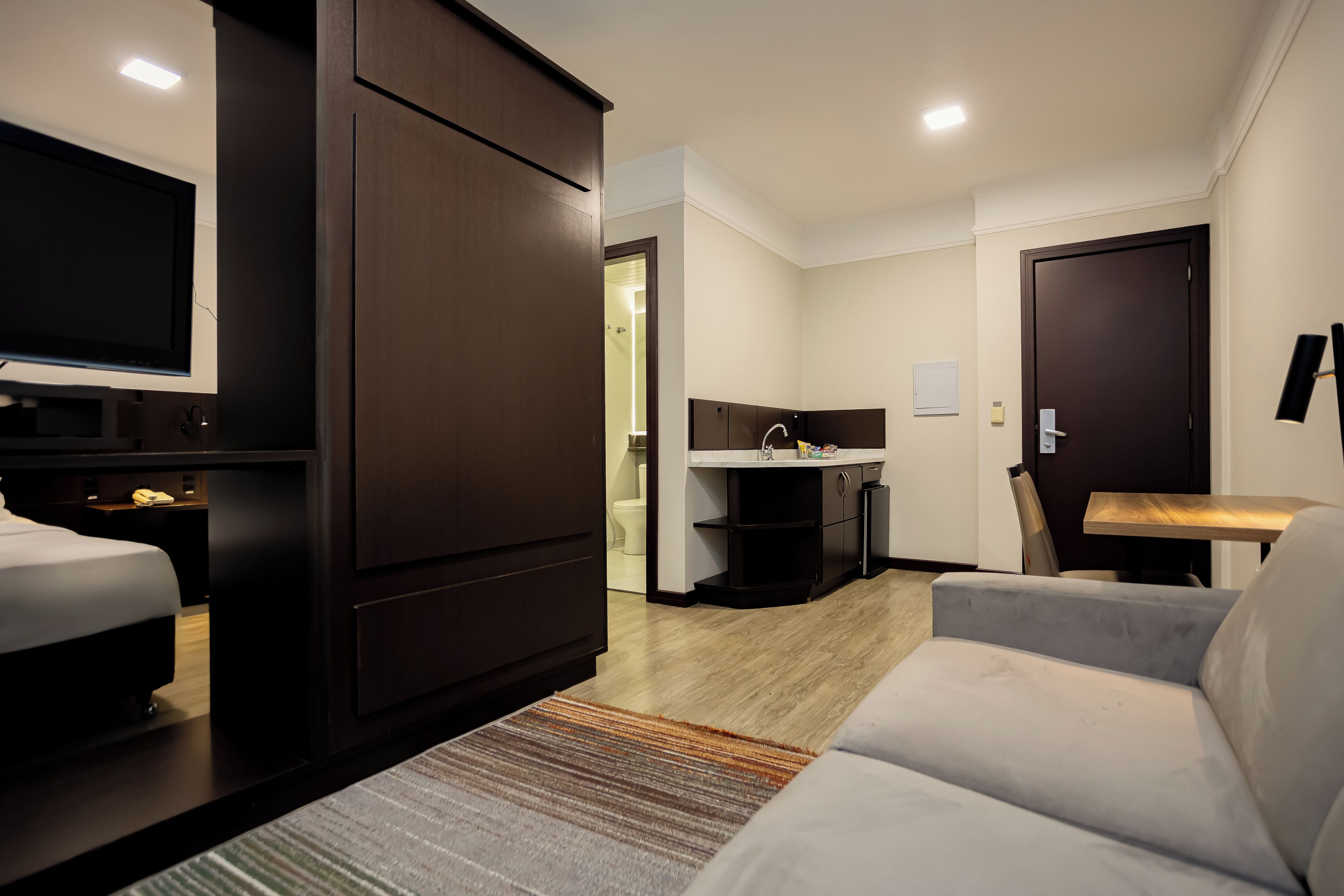 Una habitación de hotel moderna con una cama, un televisor, un sofá, un escritorio y una kitchenette.
