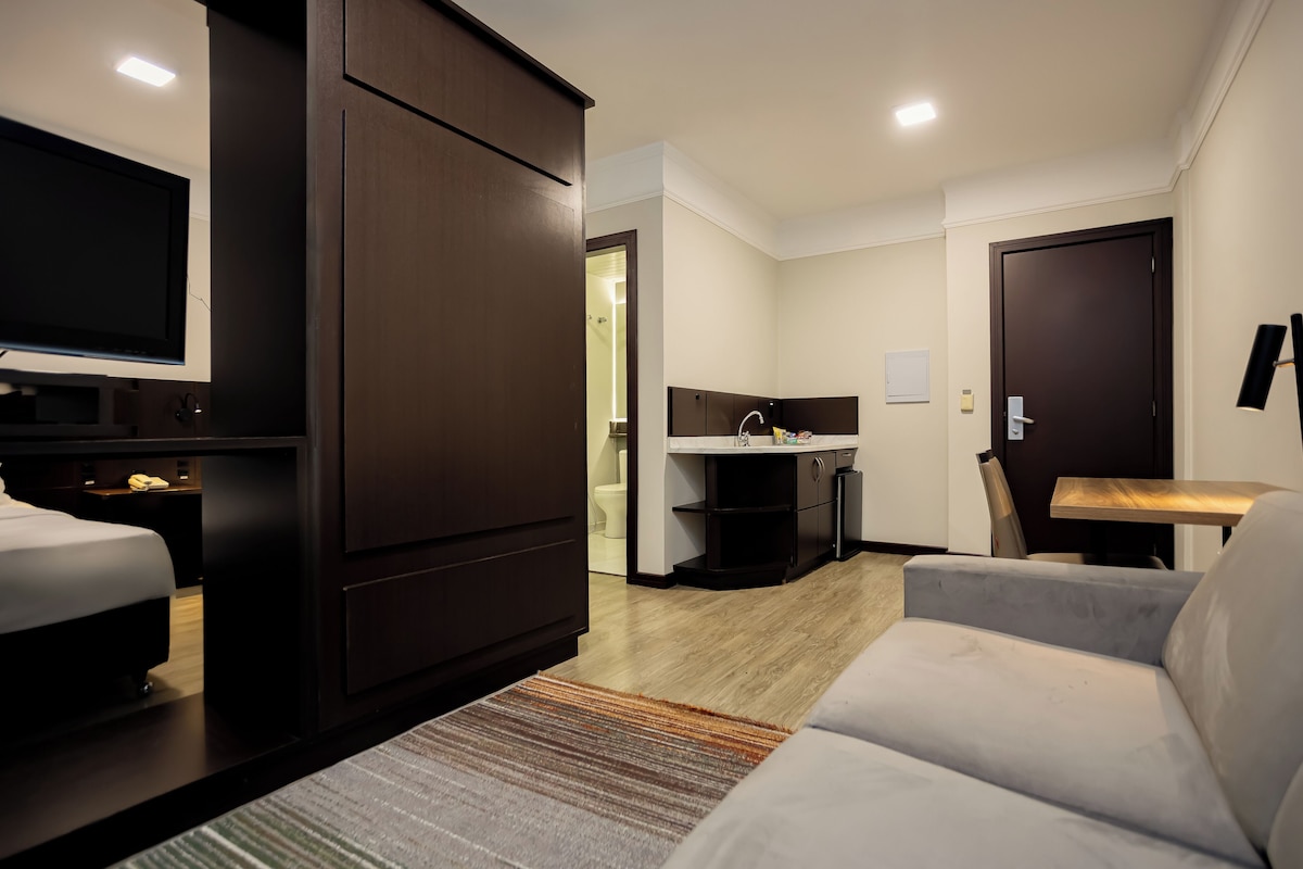 Una habitación de hotel moderna con una cama, un televisor, un sofá, un escritorio y una kitchenette.
