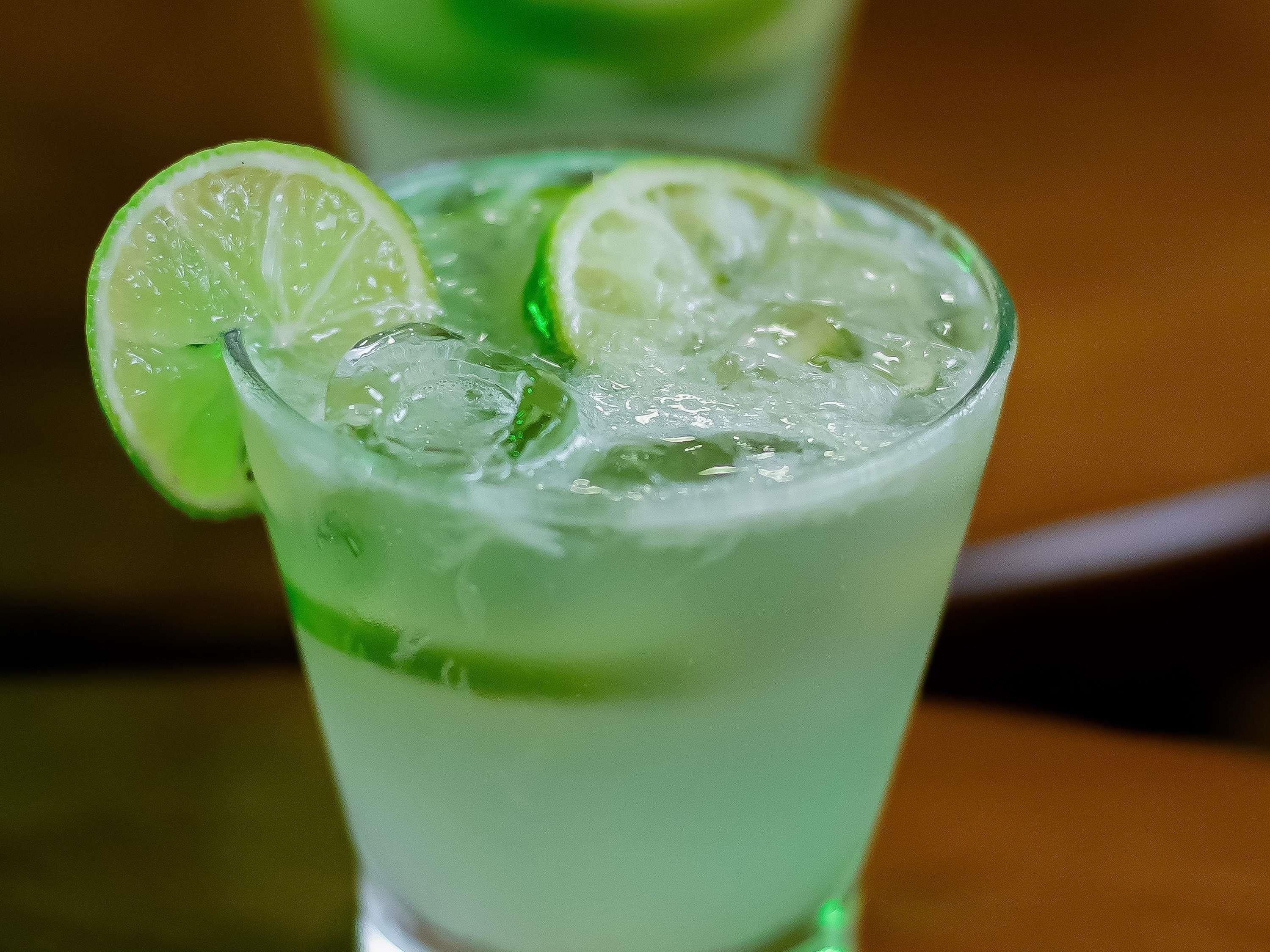 Un vaso de bebida verde con rodajas de lima y cubitos de hielo.