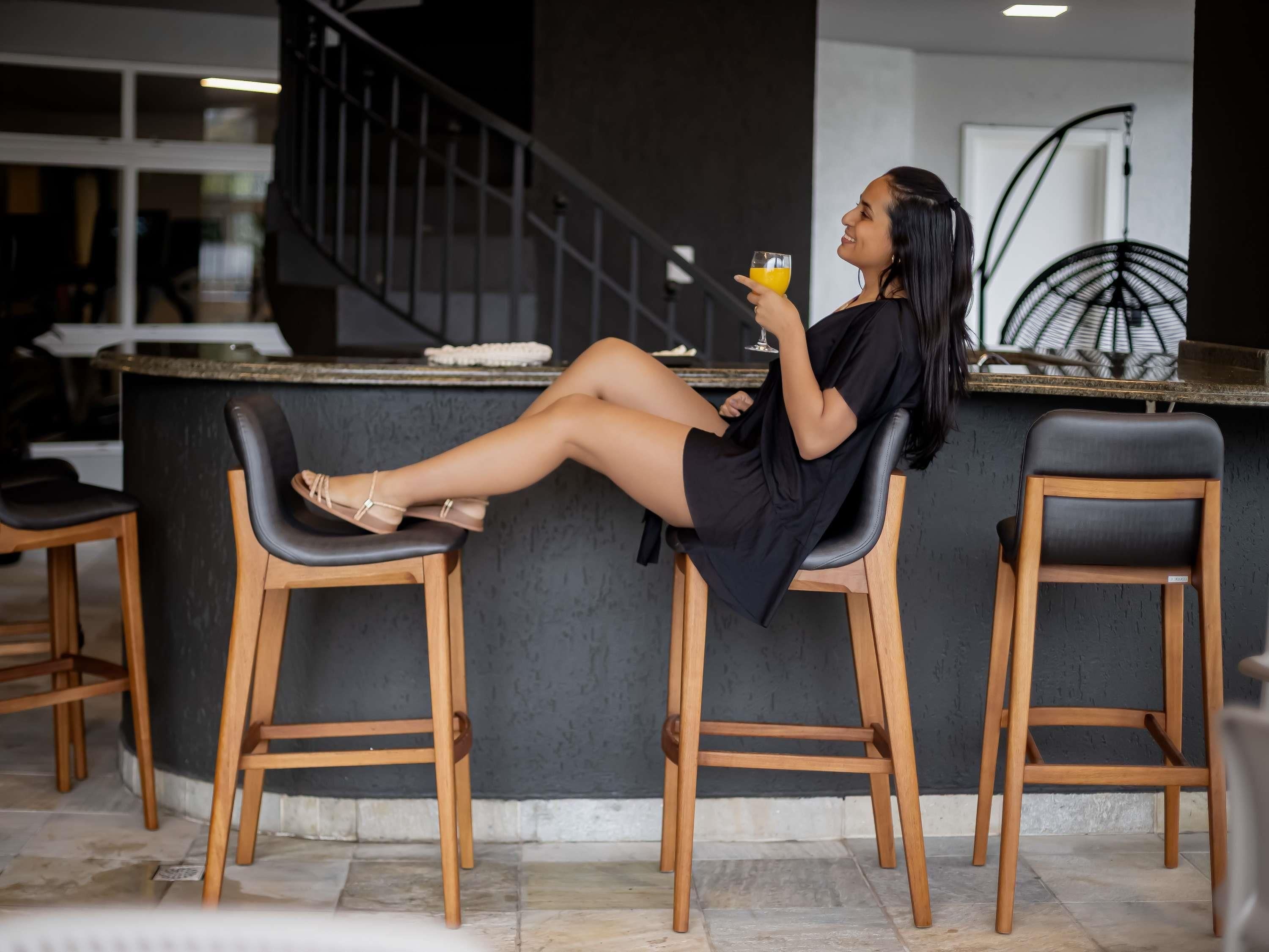 A person seated on a bar stool in a modern interior with a bar counter, wooden stools, and a staircase.
