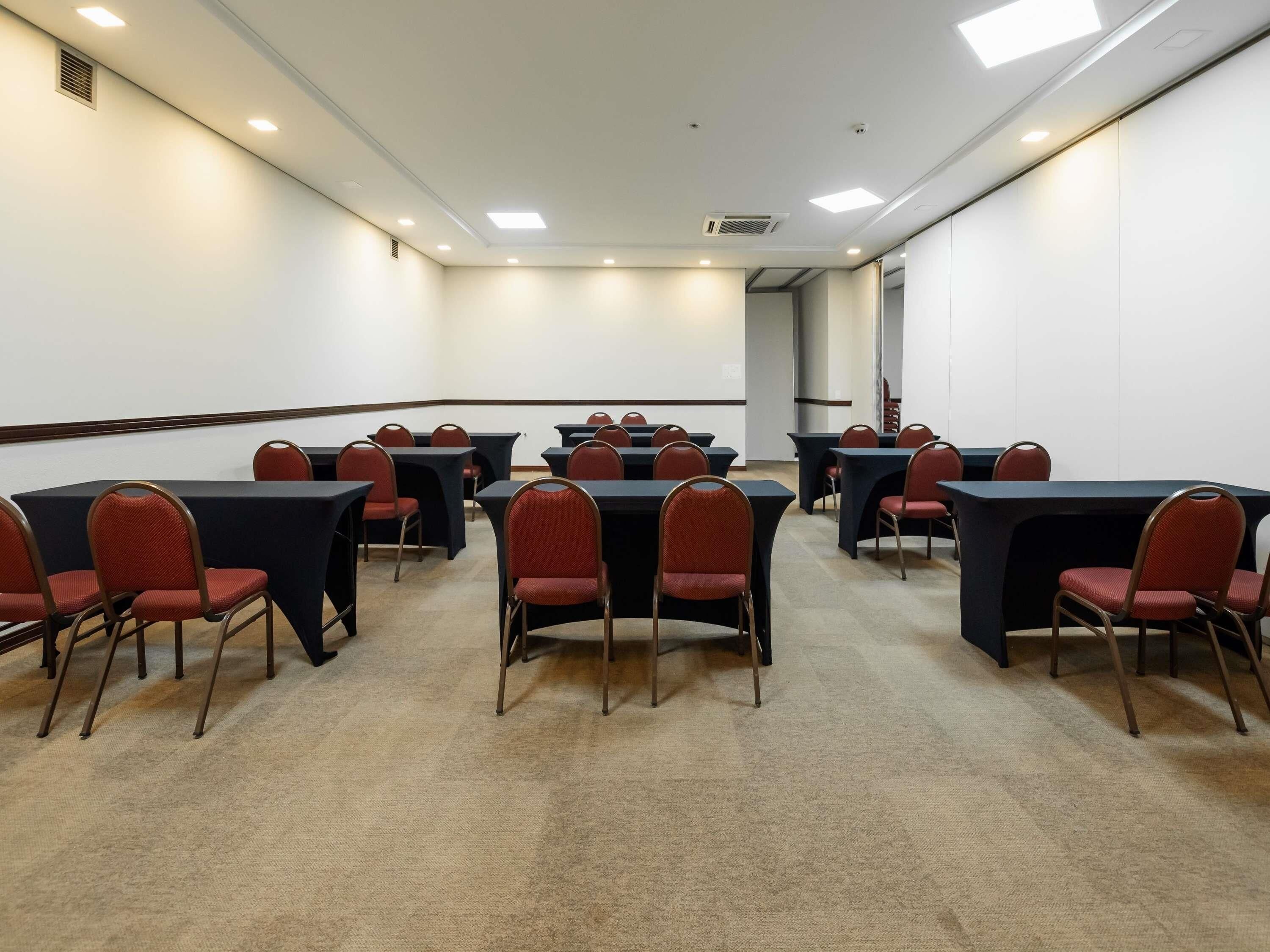 Une salle de conférence dotée de plusieurs tables et chaises, d’un sol recouvert de moquette et d’un éclairage encastré au plafond.