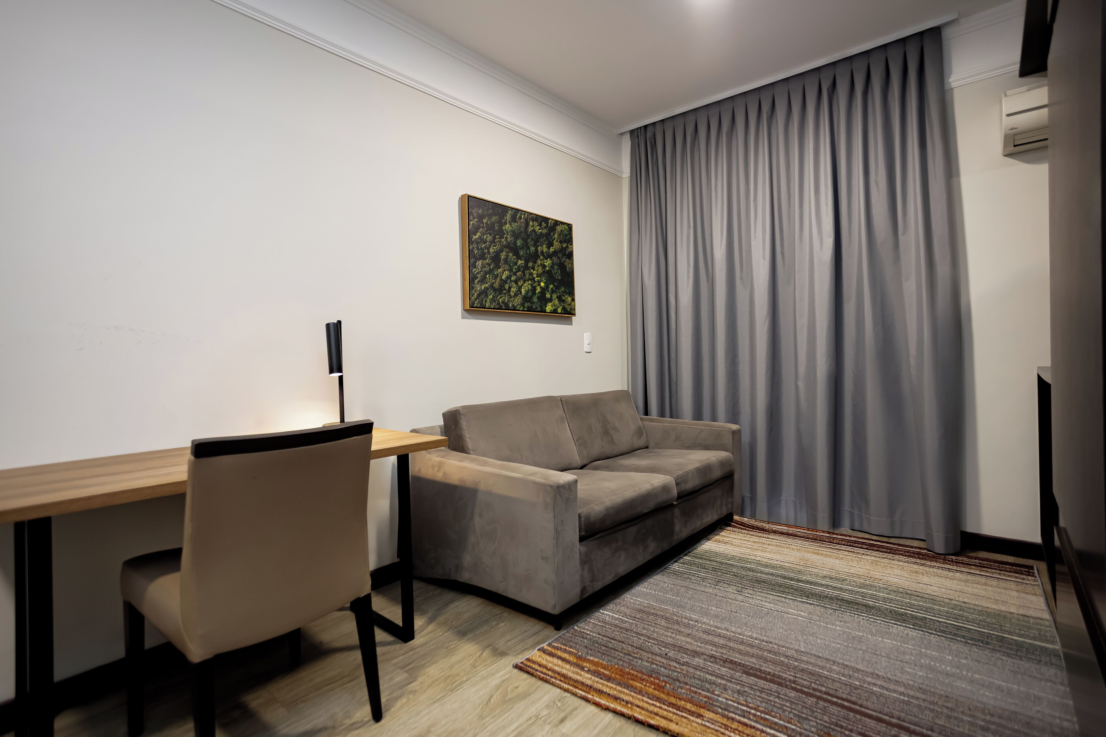 Un salon moderne avec un canapé, un bureau et une chaise. Il y a un tableau au mur et une fenêtre avec des rideaux.