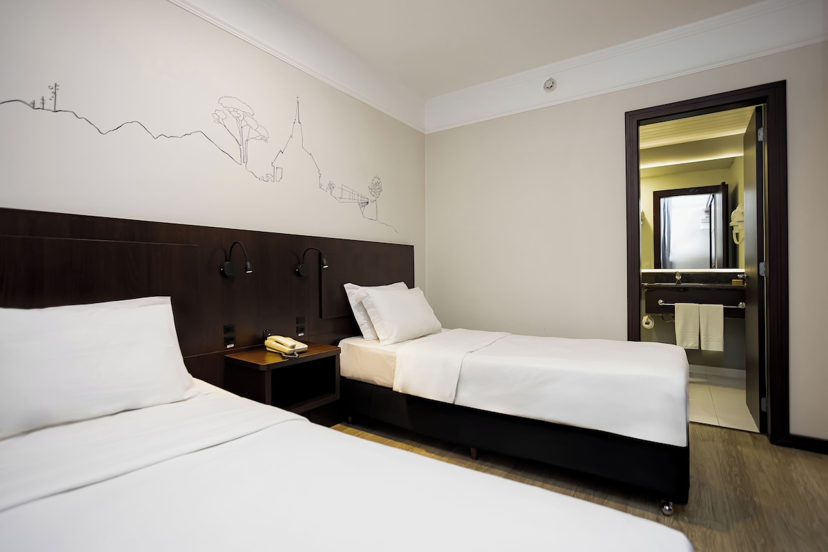 Habitación de hotel con dos camas, un cabecero de madera, una mesita de noche con un teléfono y un mural en la pared.