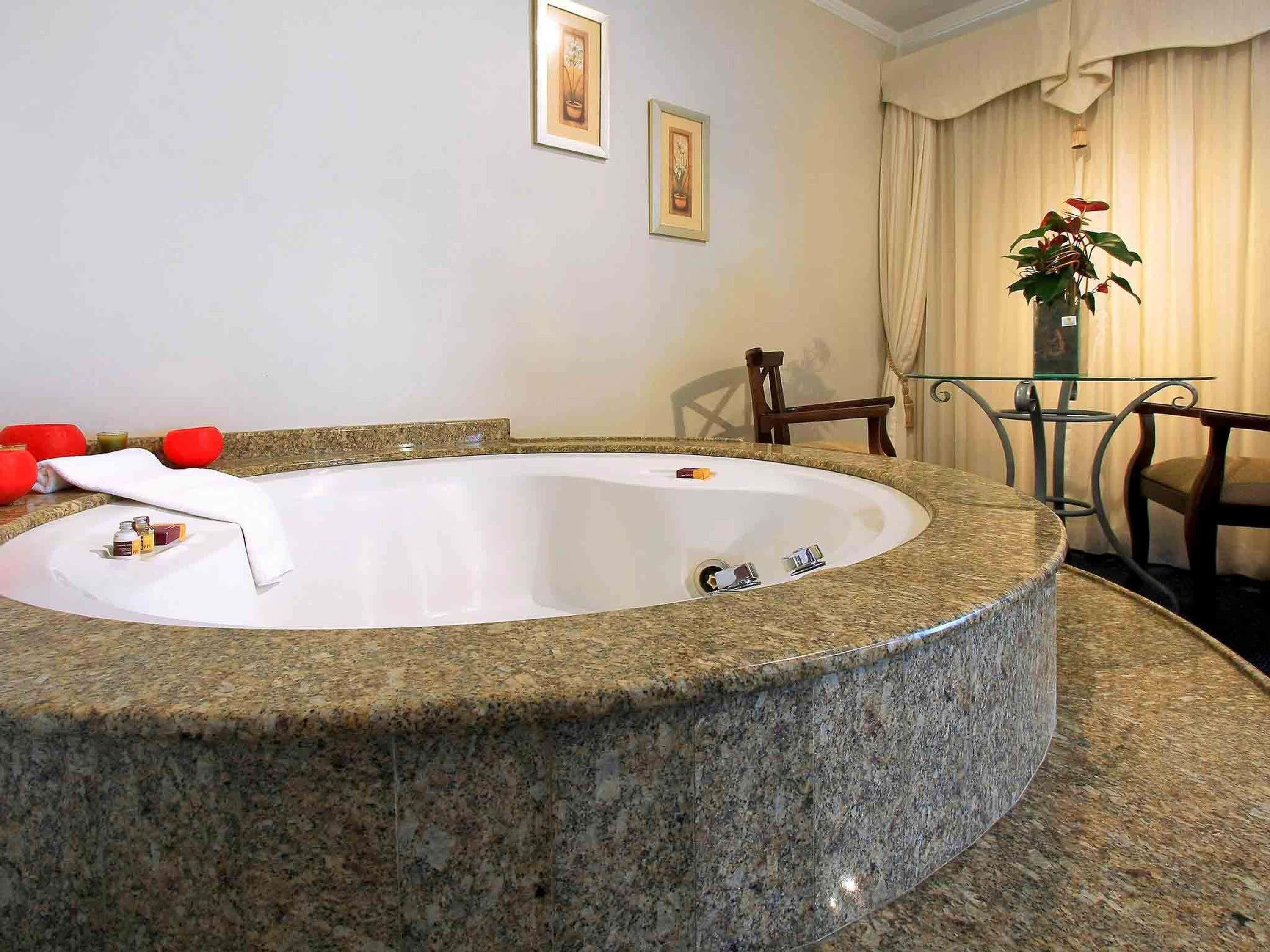 Un baño con una bañera independiente grande, una mesita con sillas y dos cuadros en la pared.