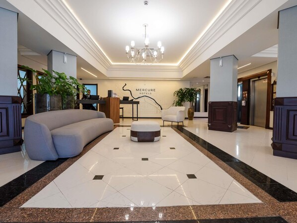 Een hotel lobby met een receptiebalie, een grote bank, een rond poef en een kroonluchter.