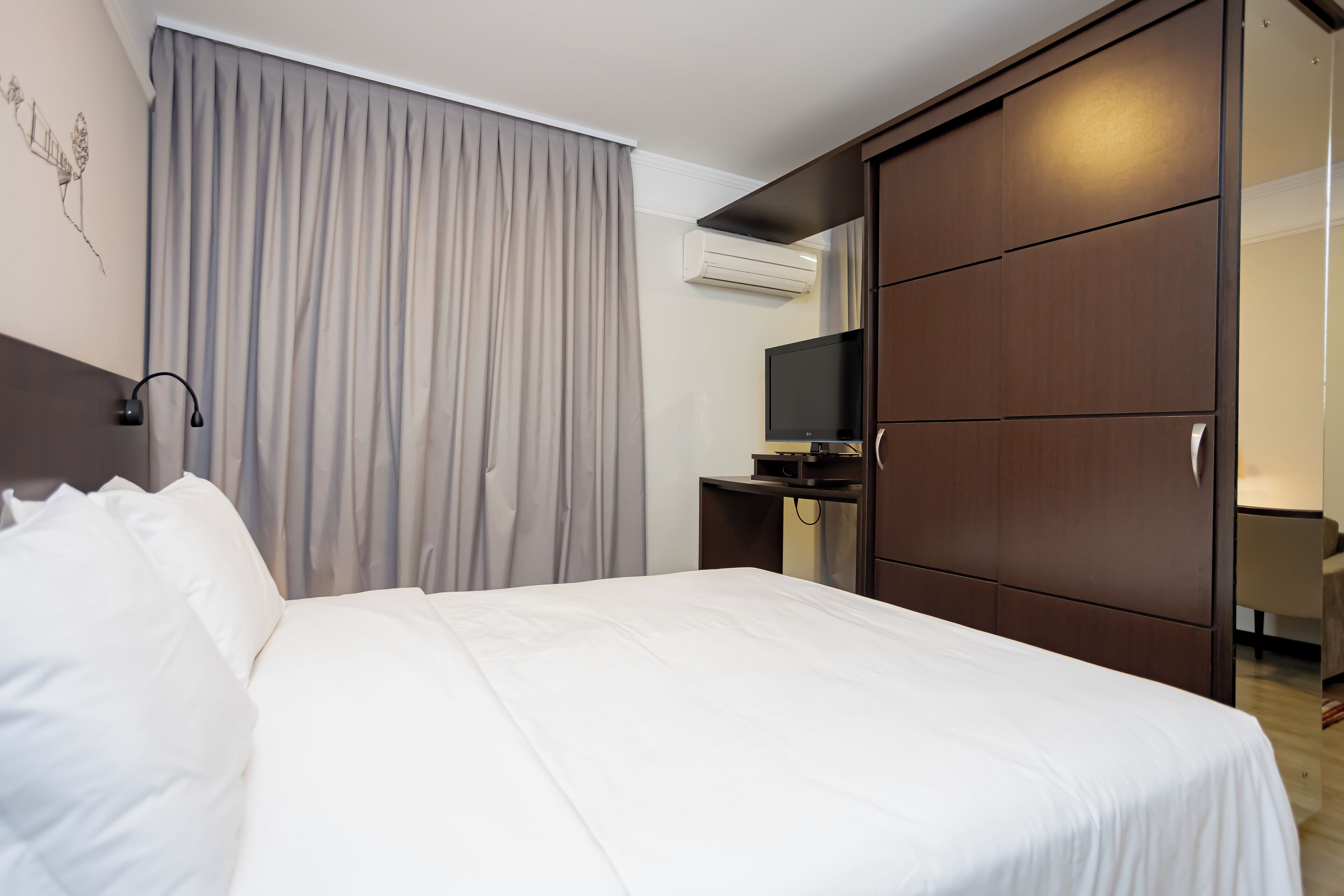 Habitación de hotel con cama, escritorio, televisor y armario.