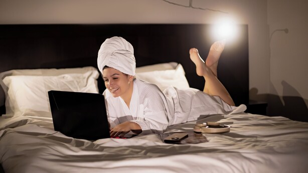 A person lying on a bed with a laptop, using a smartphone, and a remote control. - Mercure Jaraguá do Sul Hotel (Jaragua do Sul)