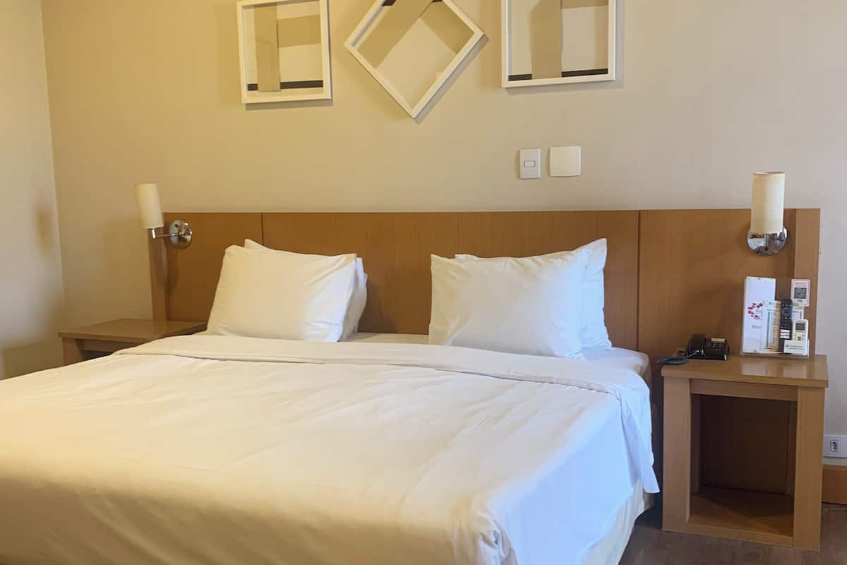 A hotel room with a large bed, two bedside tables, a wooden headboard, and wall-mounted light fixtures.