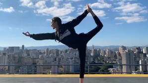 A person performing a yoga pose on an orange mat with a cityscape in the background. - Mercure Sao Paulo Bela Vista (São Paulo)