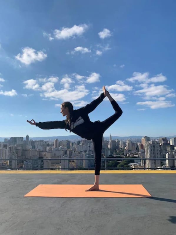 A person performing a yoga pose on an orange mat with a cityscape in the background. - Mercure Sao Paulo Bela Vista (São Paulo)
