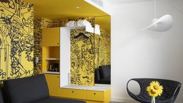 Una habitación moderna con sofá negro, detalles amarillos, una mesa blanca con un florero y una silla negra original con un girasol.