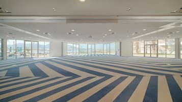 Une salle de conférence spacieuse, dotée d’un tapis à motifs, de grandes fenêtres et offrant une vue sur l’extérieur.