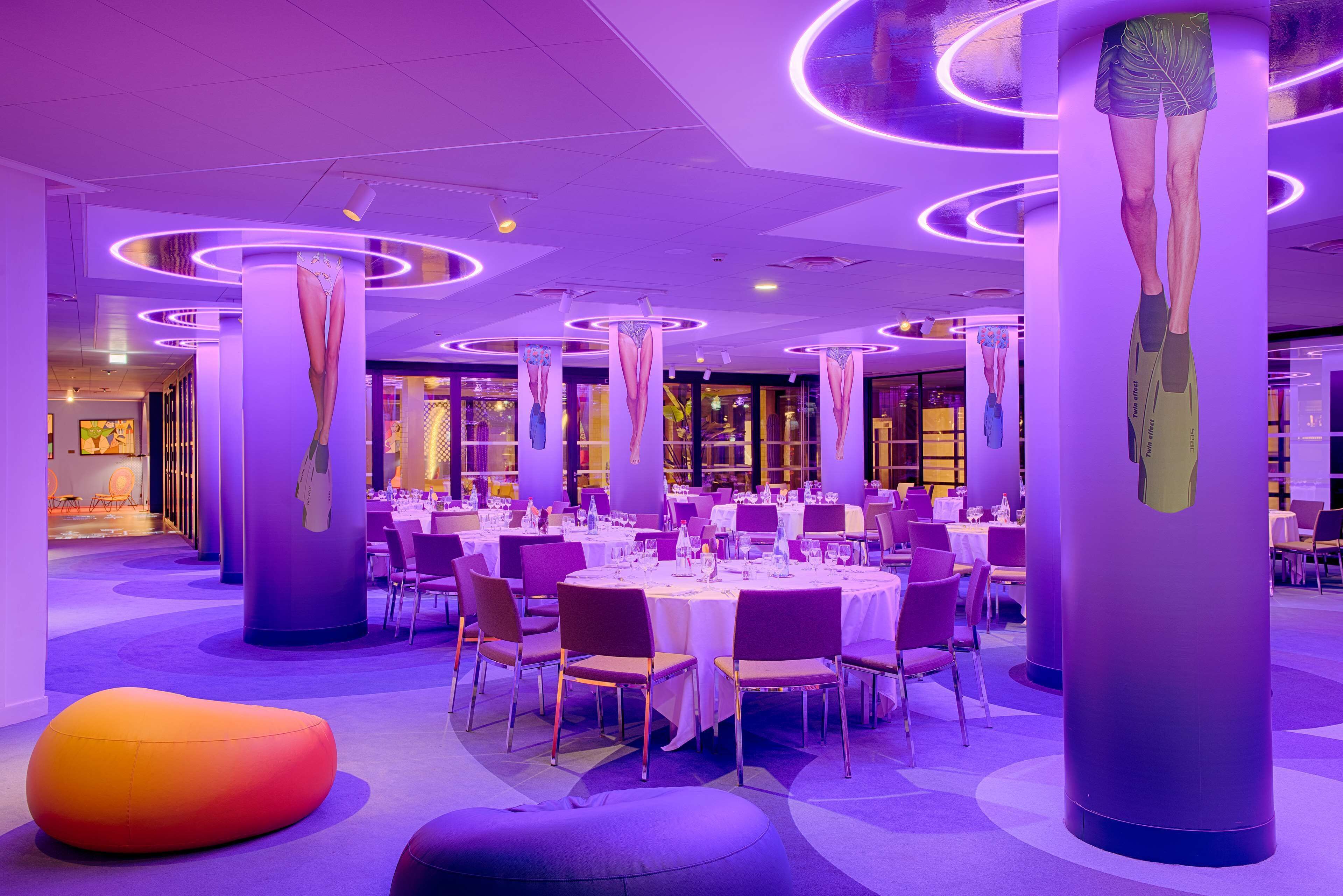 Un espace de restauration moderne avec des tables rondes, un éclairage violet et des colonnes au design original.