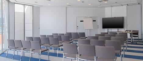 Un salón de conferencias con filas de sillas, una pantalla grande y una pizarra.